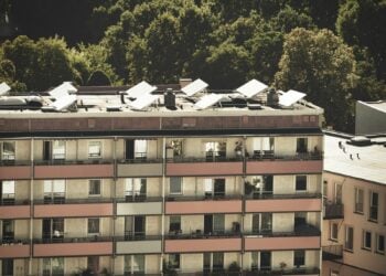 Mehrgeschossiger Wohnblock mit Balkonen, auf dem Flachdach stehen Solarkollektoren, dahinter Baumkronen