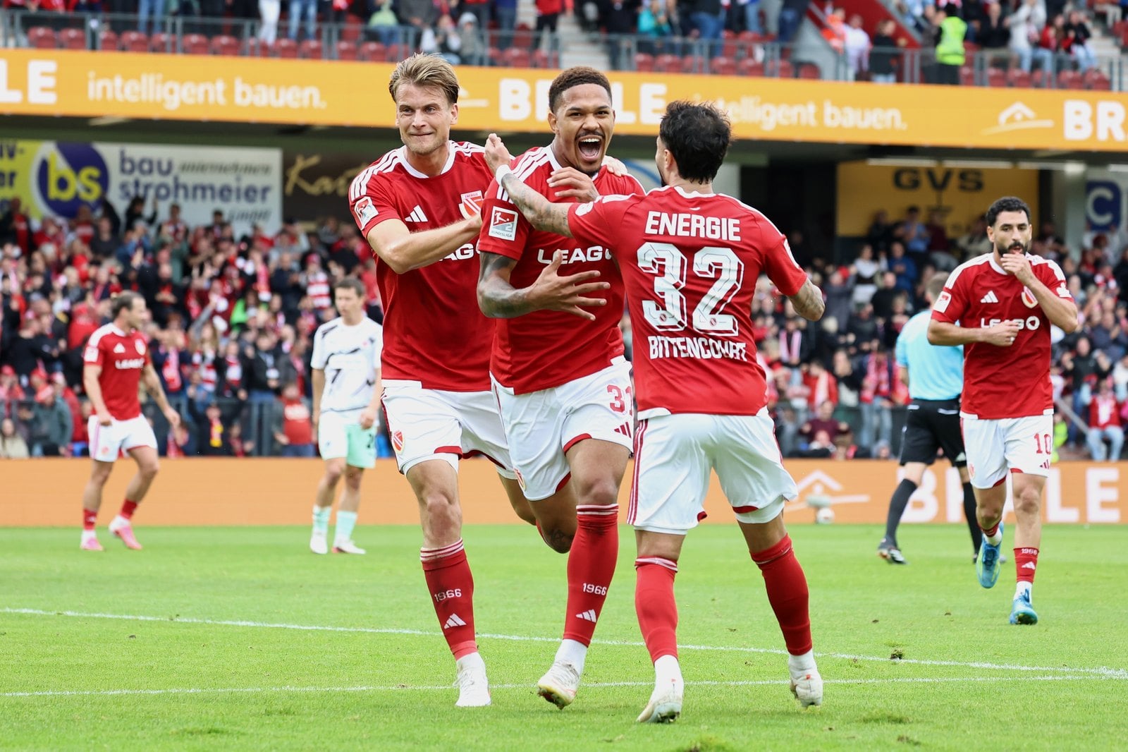 Justin Butler jubelt mit zwei Mitspielern ueber sein Tor zum 1:0