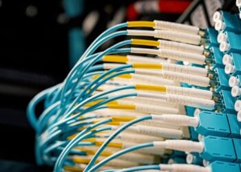 Zahlreiche türkisfarbene Glasfaserkabel mit Steckern an einem Netzwerk-Patchfeld