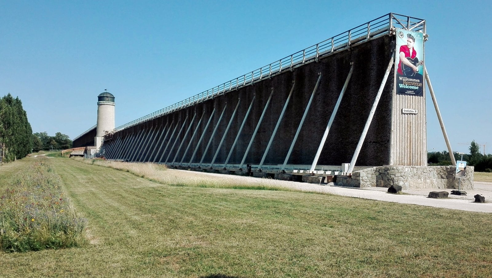Hohes hölzernes Gradierwerk mit Schwarzdornreisig in Bad Nauheim unter blauem Himmel, davor eine Wiese