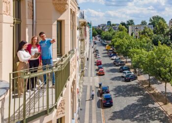 Drei Personen auf dem Balkon eines sanierten Altbaus in Cottbus, darunter eine baumgesäumte Straße