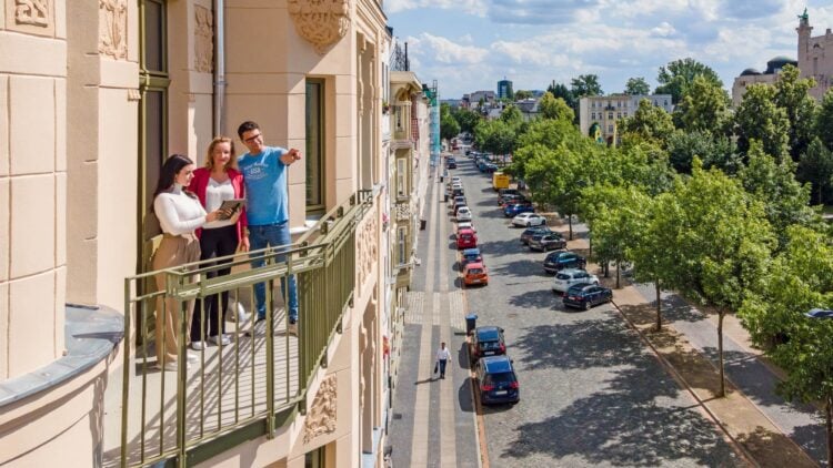 Drei Personen auf dem Balkon eines sanierten Altbaus in Cottbus, darunter eine baumgesäumte Straße