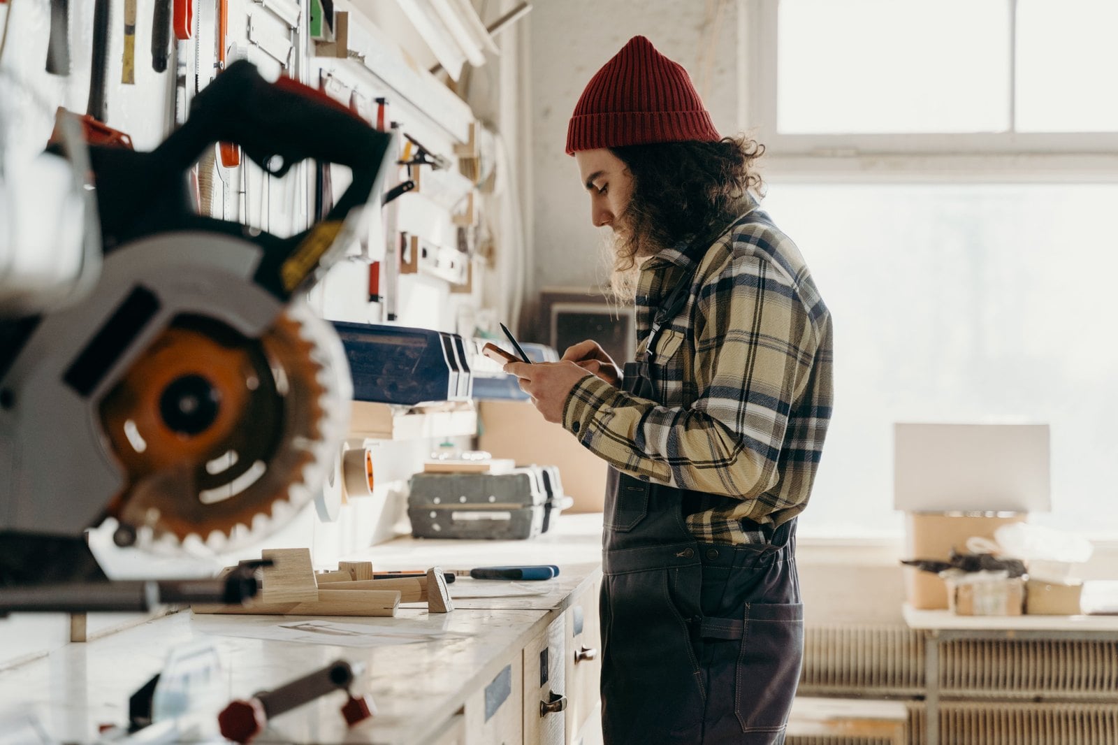 Handwerker steht mit dem Smartphone in der Hand in seiner Werkstatt