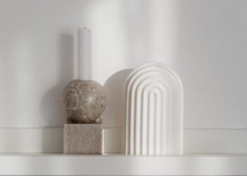 Kerzenhalter aus Stein mit weißer Kerze und eine Keramikvase auf einem hellen Wandbord