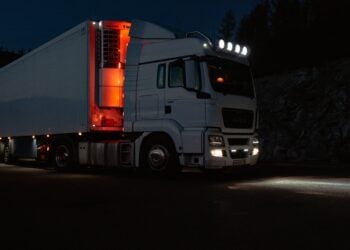 Weißer Sattelzug mit Kühlauflieger steht nachts beleuchtet an einer Straße