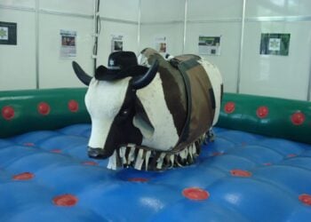 Mechanischer Rodeo-Bulle mit Cowboyhut auf einer aufblasbaren blauen Fallschutzmatte in einer Halle