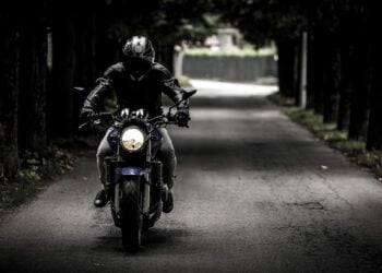 Motorradfahrer mit Integralhelm und Motorradjacke fährt auf einer von Bäumen gesäumten Straße frontal auf die Kamera zu
