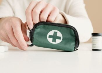 Hände öffnen eine kompakte grüne Erste-Hilfe-Tasche auf einem Tisch