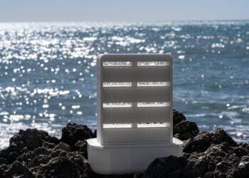 Weißes Raumklimagerät mit gitterförmiger Rieselstruktur steht auf dunklen Felsen vor dem glitzernden Meer