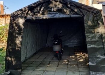 Dunkle Zeltgarage mit geöffneter Front, darin ein abgestelltes Motorrad