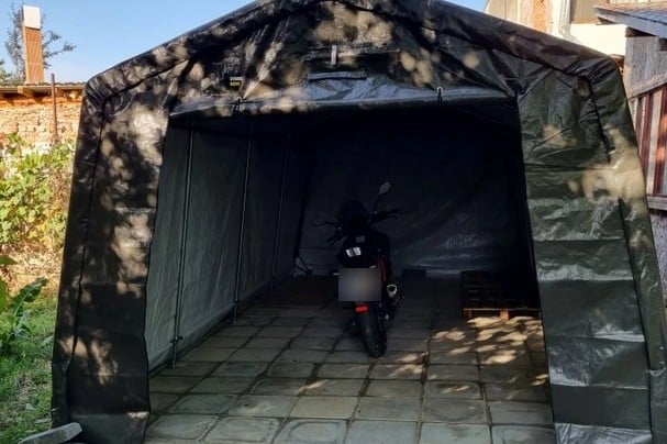 Dunkle Zeltgarage mit geöffneter Front, darin ein abgestelltes Motorrad