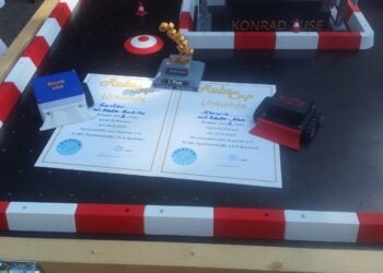 Selbst gebaute Roboter und Urkunden auf einem Spielfeld mit rot-weißer Bande beim Robo-Cup im Zuseum