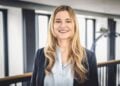 Nadine Tramowsky mit langen blonden Haaren, dunklem Blazer und hellblauer Bluse in einem hellen Gebäude