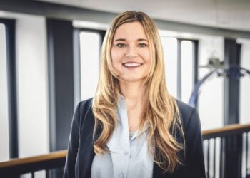Nadine Tramowsky mit langen blonden Haaren, dunklem Blazer und hellblauer Bluse in einem hellen Gebäude