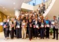 Gruppenfoto der ausgezeichneten Arbeitgeber mit Urkunden und Pokalen auf einer Treppe