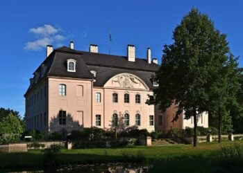 Schloss Branitz in Cottbus mit rosafarbener Fassade, Mansarddach und großem Baum vor blauem Himmel