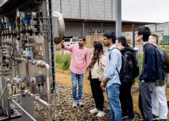 Nachwuchswissenschaftler stehen am EIZ in Cottbus vor einer technischen Anlage, einer erklärt die Technik