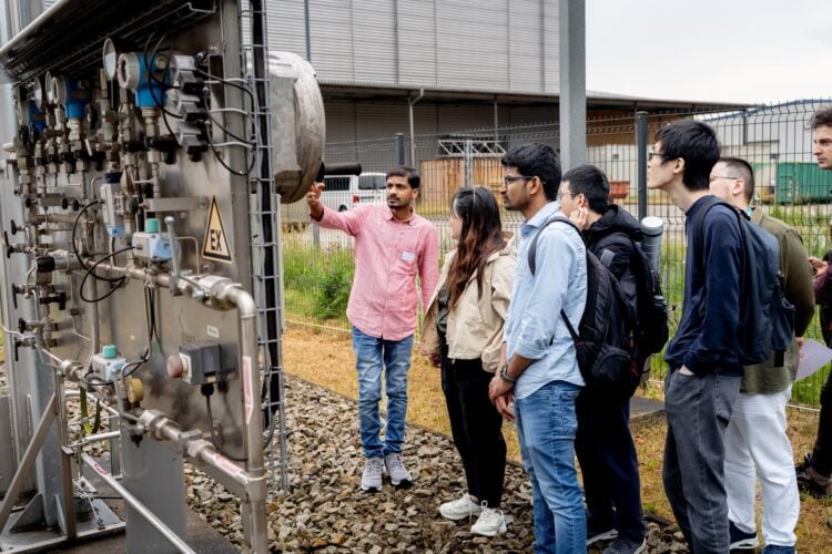 Nachwuchswissenschaftler stehen am EIZ in Cottbus vor einer technischen Anlage, einer erklärt die Technik