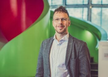 André Wendler mit Brille und Sakko vor der roten und grünen Wendeltreppe im IKMZ in Cottbus