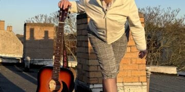 Künstlerin Ekna aus Berlin mit Schiebermütze und Akustikgitarre auf einem Dach