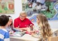 Ehrenamtliche in rotem Johanniter-Shirt sitzt mit drei Kindern an einem Tisch