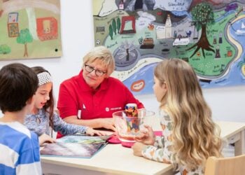 Ehrenamtliche in rotem Johanniter-Shirt sitzt mit drei Kindern an einem Tisch