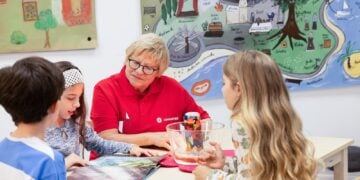 Ehrenamtliche in rotem Johanniter-Shirt sitzt mit drei Kindern an einem Tisch