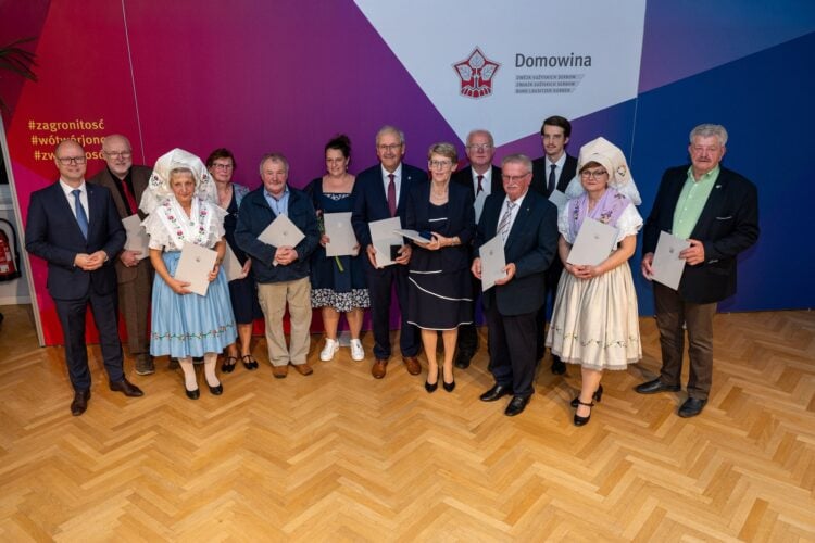 Gruppenfoto der Geehrten mit Urkunden, zwei Frauen in sorbischer Tracht, vor einer Wand mit Domowina-Logo