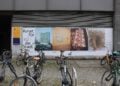 Großformatige Plakatwand mit Schriftzug Kunst für die Stadt und mehreren Fotografien, davor abgestellte Fahrräder