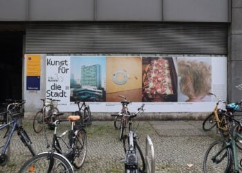 Großformatige Plakatwand mit Schriftzug Kunst für die Stadt und mehreren Fotografien, davor abgestellte Fahrräder