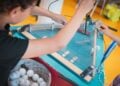 Ein Kind baut an einem selbstgebauten Spieltisch aus Holz und Plexiglas, daneben ein Korb mit beschrifteten Bällen