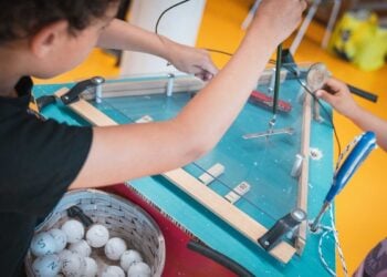 Ein Kind baut an einem selbstgebauten Spieltisch aus Holz und Plexiglas, daneben ein Korb mit beschrifteten Bällen