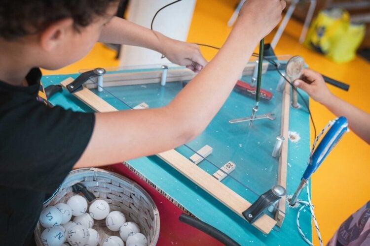 Ein Kind baut an einem selbstgebauten Spieltisch aus Holz und Plexiglas, daneben ein Korb mit beschrifteten Bällen