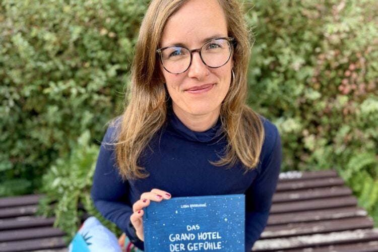 Lea Sattler sitzt auf einer Bank und hält das Buch Das Grand Hotel der Gefühle