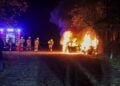 Feuerwehrleute vor einem brennenden Auto auf dem Parkplatz am Madlower Badesee in Cottbus