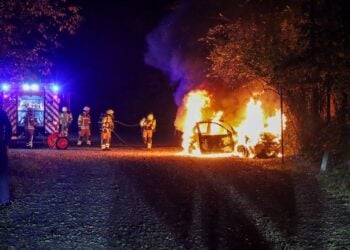 Feuerwehrleute vor einem brennenden Auto auf dem Parkplatz am Madlower Badesee in Cottbus