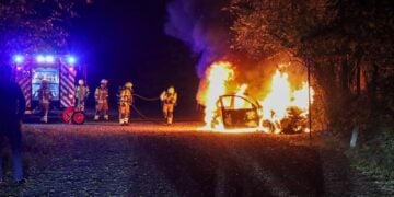 Feuerwehrleute vor einem brennenden Auto auf dem Parkplatz am Madlower Badesee in Cottbus