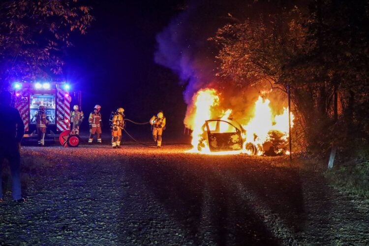 Feuerwehrleute vor einem brennenden Auto auf dem Parkplatz am Madlower Badesee in Cottbus