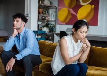 Ein Mann und eine Frau sitzen nachdenklich und voneinander abgewandt auf einem Sofa