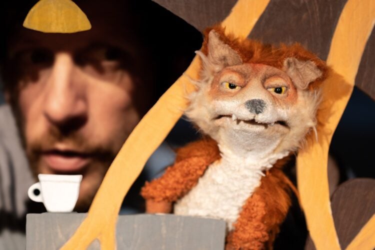Puppenspieler im Hintergrund, im Vordergrund eine Fuchs-Handpuppe in einer Bühnenkulisse