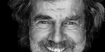 Schwarz-Weiß-Porträt von Reinhold Messner mit grauem Bart und lockigem Haar, lachend