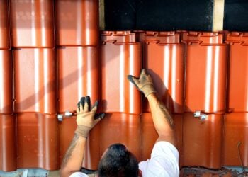 Ein Dachdecker legt rote Dachpfannen auf ein Dach