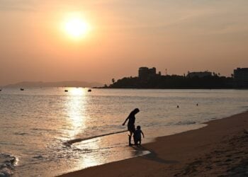 Silhouetten eines Erwachsenen und eines Kindes am Strand im Abendlicht