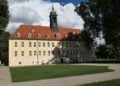 Schloss Elsterwerda mit Uhrturm, davor Rasenfläche und Parkwege