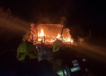 Feuerwehrleute mit Helmen vor einer brennenden Gartenlaube in Finsterwalde bei Nacht
