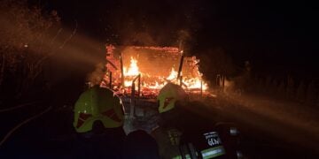 Feuerwehrleute mit Helmen vor einer brennenden Gartenlaube in Finsterwalde bei Nacht
