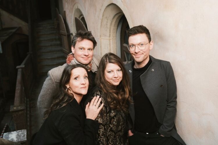 Die vier Musiker von Christmas 4 Friends, zwei Frauen und zwei Männer, vor einer hellen Wand