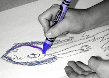 Kinderhand malt mit einem lila Wachsmalstift ein Gesicht auf Papier