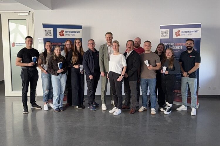 Gruppenfoto von 15 Personen in einem hellen Raum vor zwei Aufstellern des Rettungsdienstes Spree-Neiße