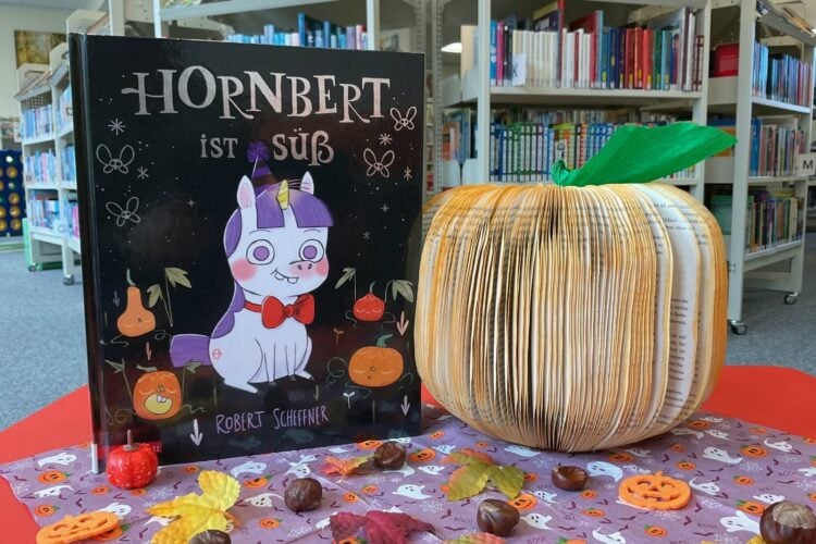 Bilderbuch Hornbert ist süß neben einem aus Buchseiten gefalteten Kürbis vor Bücherregalen